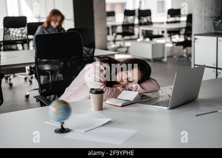 Ein müder Student schläft auf dem Schreibtisch neben dem Laptop und dem Papierbecher Stockfoto