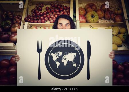 Globaler Hunger, Nahrungsmittelversorgung. Schockierter Mann, der ein Warnsignal vor einem Lebensmittelgeschäft hält. Weltkarte in einem Teller mit Messer und Gabel. Stockfoto