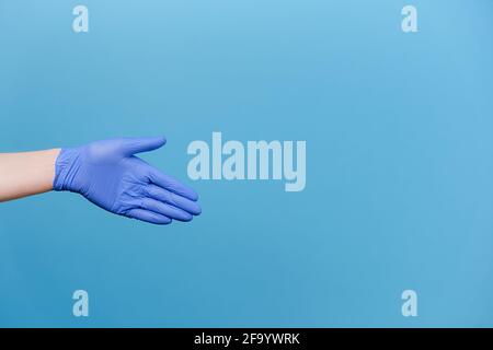 Willkommensgeste. Offene Handfläche. Nahaufnahme einer nicht erkennbaren männlichen Hand in medizinischen Schutzhandschuhen, isoliert auf blauem Hintergrund mit Kopierraum Stockfoto