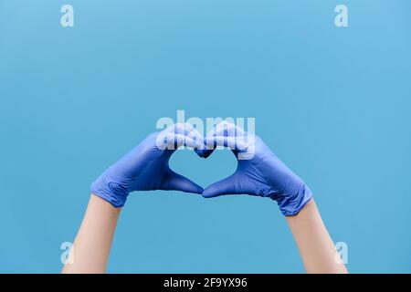 Nahaufnahme der männlichen Hände in medizinischen Schutzhandschuhen, die ein Herzsymbol bilden, um Ärzten und Krankenschwestern für ihre Hilfe zu danken Stockfoto