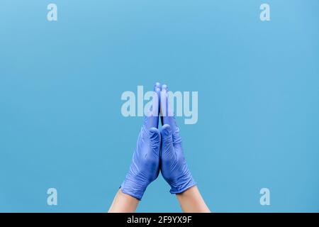 Nahaufnahme eines nicht erkennbaren Mannes in medizinischen Schutzhandschuhen hält Hände im Gebet zu gott, meditierend, für Gesundheit betend, isoliert auf blauem Hintergrund Stockfoto