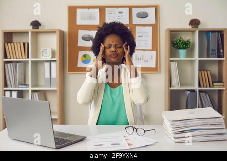 afroamerikanische Geschäftsfrau, die sich die Tempel reiben, sitzt auf dem Büroschreibtisch Stockfoto