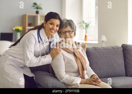 Porträt eines lächelnden jungen Arztes oder einer Krankenschwester zu Hause, die sich umarmt Ihre ältere Patientin Stockfoto