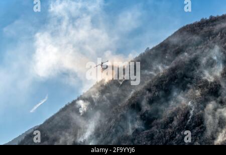 Löschflugzeuge, die das Wasser fallen lassen, um einen Brand auf einem Berg über dem Ghirla-See in Valganna, Provinz Varese, Italien, zu bekämpfen Stockfoto