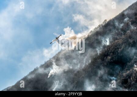 Löschflugzeuge, die das Wasser fallen lassen, um einen Brand auf einem Berg über dem Ghirla-See in Valganna, Provinz Varese, Italien, zu bekämpfen Stockfoto