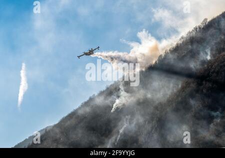 Löschflugzeuge, die das Wasser fallen lassen, um einen Brand auf einem Berg über dem Ghirla-See in Valganna, Provinz Varese, Italien, zu bekämpfen Stockfoto