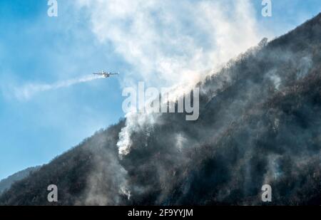 Löschflugzeuge, die das Wasser fallen lassen, um einen Brand auf einem Berg über dem Ghirla-See in Valganna, Provinz Varese, Italien, zu bekämpfen Stockfoto