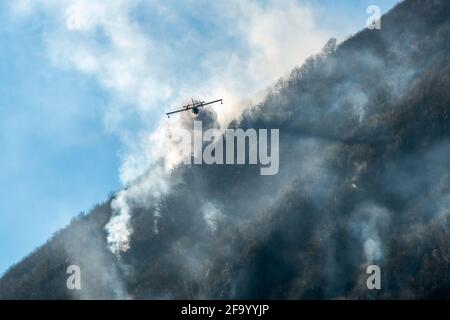 Löschflugzeuge, die das Wasser fallen lassen, um einen Brand auf einem Berg über dem Ghirla-See in Valganna, Provinz Varese, Italien, zu bekämpfen Stockfoto