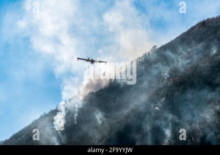 Löschflugzeuge, die das Wasser fallen lassen, um einen Brand auf einem Berg über dem Ghirla-See in Valganna, Provinz Varese, Italien, zu bekämpfen Stockfoto