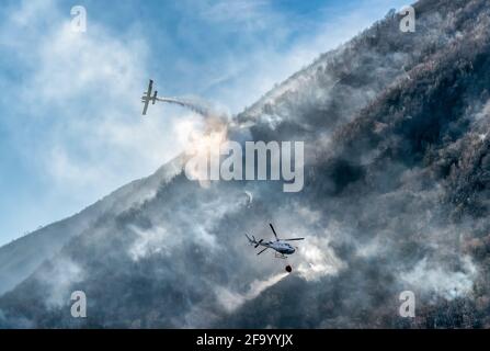 Feuerwehrflugzeuge und Hubschrauber, die das Wasser fallen lassen, um einen Brand auf dem Berg, oberhalb des Ghirla-Sees in Valganna, Provinz Varese, Italien, zu bekämpfen Stockfoto