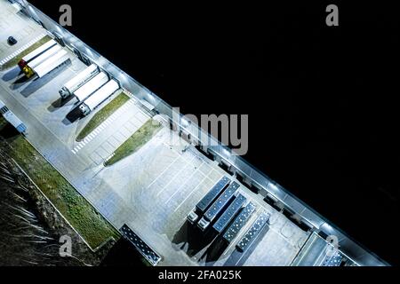 Luftaufnahme der Lastkraftwagen beim Entladen im Logistikzentrum. Nachtsicht.LKW entladen im Logistikzentrum. Drohnenfotografie. Stockfoto