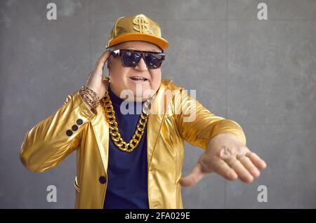 Lustiger älterer Mann in goldener Jacke, Baseballmütze und Kette, der Musik auf der Disco-Party spielt Stockfoto