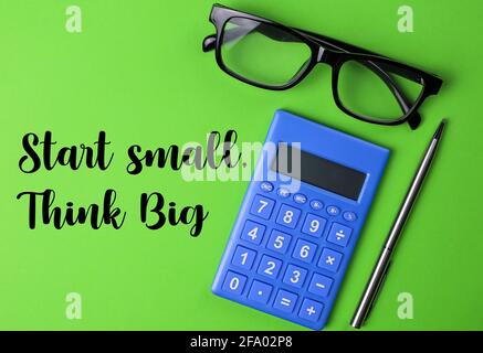 Draufsicht auf Brille, Rechner und Stift mit geschriebenem Text Start Small Think Big auf grünem Hintergrund geschrieben. Bildung und Geschäftskonzept Stockfoto