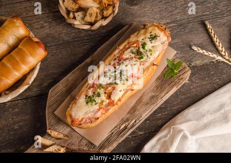 Laib gefüllt mit Käse und Tomaten auf einem hölzernen Hintergrund mit Zutaten, Fast Food Stockfoto