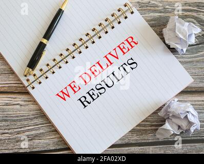 Draufsicht auf ein Notizbuch und einen Stift mit We Deliver Ergebnisse auf dem Notizbuch geschrieben Stockfoto