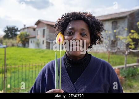Porträt einer schönen afroamerikanischen Frau mittleren Alters, die lächelt Und hielt eine gelbe Tulpe nahe an ihre Wange Stockfoto