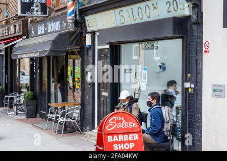 Kunden, die vor dem Saloon, einem Friseurladen an der King's Cross Road, warten, öffnen am ersten Tag der Lockerung im April 2021 in London, Großbritannien Stockfoto