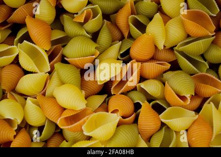 Nahaufnahme einer Mischung aus Pastaschalen Conchiglie Rigate in drei Farben: Gelb, grün und rot mit dem Zusatz von Spinat und Tomaten als Hintergrund Stockfoto