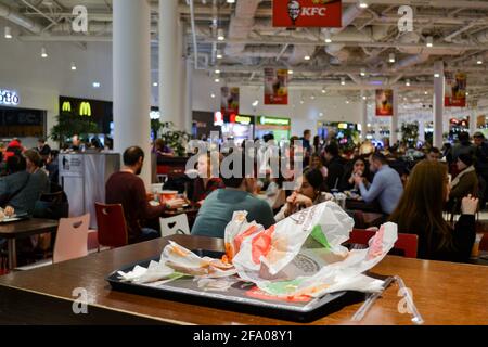 Russland, 2019. November: Nahaufnahme eines Tabletts mit Essensresten, Papierverpackungen von Hamburgern auf einem verschwommenen Hintergrund von Menschen, die auf einem Food Court essen Stockfoto