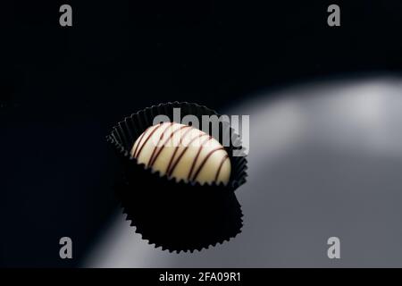 Single milk chocolate Candy in black paper stand isoliert auf glasierte Oberfläche. Seitenansicht, Nahaufnahme, Platz für Text Stockfoto