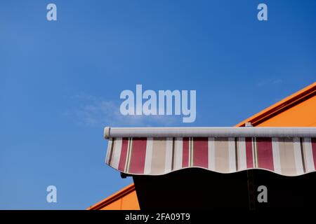 Einlauffähige Markise oder Zelt aus Segeltuch. Sonne- und UV-Schutz-Konzept. Blick in den hohen Winkel. Klarer blauer Himmel. Weiße Wolke. Heißer, klarer Sommertag. Regenfest. Stockfoto