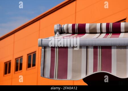Einrackbarer Segeltuchvorzelt, Sonnenschutz. Blick aus hohem Winkel. Klarer blauer Himmel. Weiße Wolke. UV-Schutz. Heißer klarer Sommertag. Orangefarbene Gebäudefassade Stockfoto