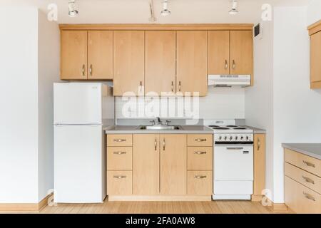 Eine Ahornküche in einer leeren Stadtwohnung mit weißen Geräten, Granitplatten, vielen Schränken für die Aufbewahrung und Hartholzböden. Stockfoto