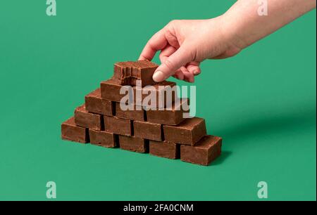 Minimalistischer Schuss mit der Hand einer Frau, die einen Schokoladen-Fudge-Riegel greift. Stapel von Fudge Bars isoliert auf einem grünen Hintergrund. Stockfoto