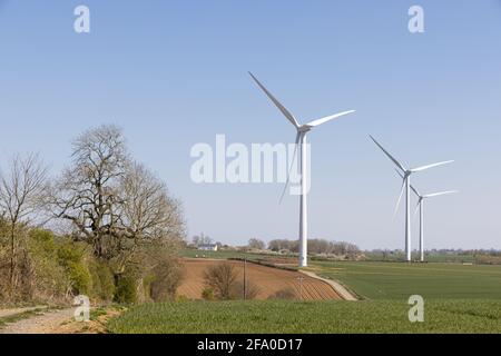 Crick, Northamptonshire, Großbritannien - 19. April 2021: Drei Windturbinen stehen in Ackerland unter einem klaren blauen Himmel. Stockfoto