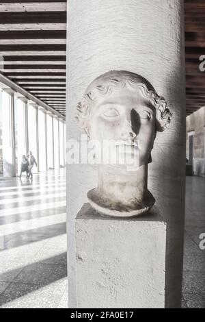 Antikes griechisches Büste auf Sockel in der Nähe der Akropolis in Athen, Griechenland Mit unkenntlichen Touristen, die durch die Schatten der Säulen laufen Stockfoto