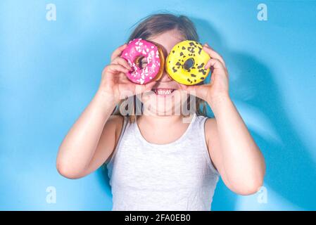 Kleine glückliche lustige Mädchen mit bunten Zucker glasiert rosa und gelben Donuts, Urlaub, Glück, Sommerurlaub Konzept, Stockfoto