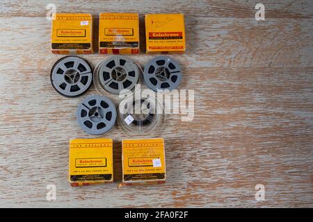 Fünf geladene Kodak 8-mm-Folienspulen mit gelben Versandkartons, die auf einer grau lackierten Oberfläche mit Holzmaserung angeordnet sind Stockfoto