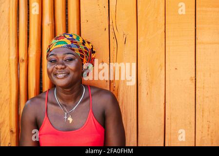 Afrikanische Frau mit einem hoffnungsvollen glücklichen Lächeln, das gegen eine steht Bemalte Holzwand im tropischen Dorf Keta Ghana Westafrika Stockfoto