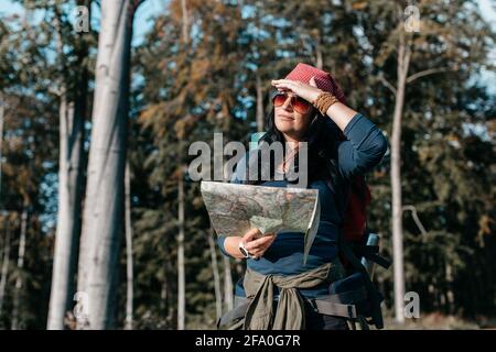 Eine Frau mit einem Rucksack, die eine Karte überprüft. Eine Wanderin, die im Wald unterwegs ist und nach dem Weg sucht. Stockfoto