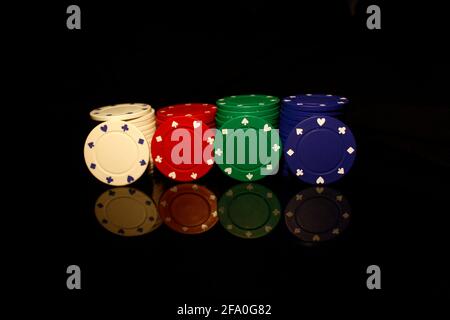 Weiße, rote, grüne, blaue Pockerchips stapeln mit vier Chips vorne isoliert auf schwarz mit Reflexion Stockfoto