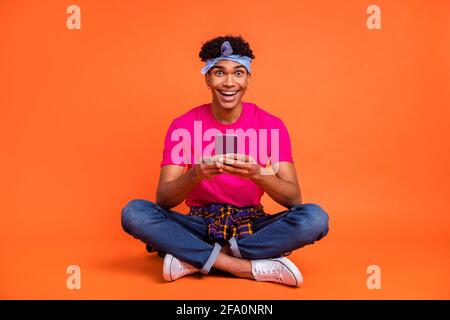 In voller Länge Körpergröße Foto von staunenden Kerl lesen Nachrichten Mit Handy lachen isoliert lebendige orange Farbe Hintergrund Stockfoto