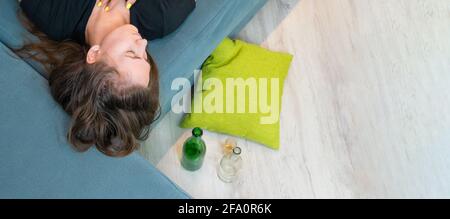 Betrunkene junge dunkelhaarige Frau schläft nach einer Party oder Stress mit leeren Flaschen auf dem Boden auf der Couch, Draufsicht aus dem Kopierraum. Banner Stockfoto