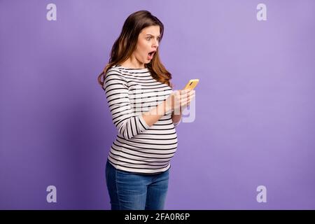 Foto von schockiert Frau erwartet Kind tragen gestreiften Hemd Bauch Offener Mund Typisierung moderne Gerät isoliert lila Farbe Hintergrund Stockfoto