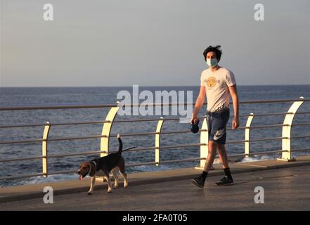 Beirut, Libanon. April 2021. Ein Mann mit Gesichtsmaske geht am 21. April 2021 auf einer Promenade entlang der Küste in Beirut, Libanon, mit einem Hund spazieren. Der Libanon meldete am Mittwoch 32 Todesfälle durch COVID-19, was die Zahl der Todesopfer auf 7,027 erhöht, teilte das Gesundheitsministerium mit. Das Ministerium meldete auch 2,082 neue Fälle, so dass die Zahl der Infektionen auf 515,088 annahm. Quelle: Liu Zongya/Xinhua/Alamy Live News Stockfoto