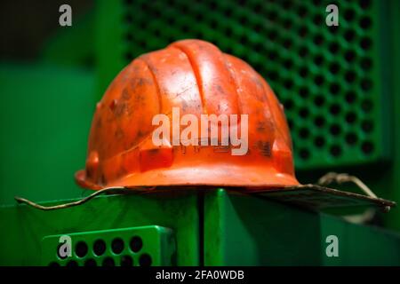 Abstract Industrie Foto.Orange Arbeit Helm auf grünen Metall Maschinenabdeckung.Close-up.Low Tiefenschärfe, Hardhat im Fokus.Produktionsanlage. Stockfoto