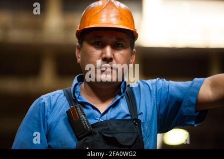 Porträt eines jungen asiatischen Arbeiters in orangefarbenem Helm und schwarzem Overall. Anlagen für die Gas- und Ölindustrie. Ust-Kamenogorsk, Kasachstan. Stockfoto