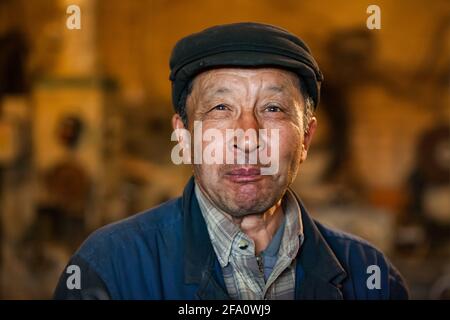 Ust'-Kamenogorsk, Kasachstan. Fabrik Vostokmashzavod. Porträt eines erwachsenen asiatischen Arbeiters in schwarzer Mütze. Nahaufnahme. Unscharfer brauner Hintergrund Stockfoto