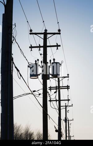 Reihe von verketteten Strommasten mit elektrischen Übertragungsleitungen und Transformatoren bei Sonnenaufgang Stockfoto