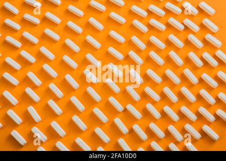 Reihen weißer Arzneitabletten auf orangefarbenem Hintergrund Stockfoto