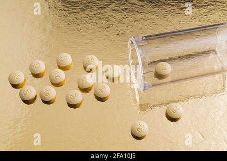 Gelbe Arzneitabletten und klare Plastikflasche auf glänzendem Gold Hintergrund Stockfoto