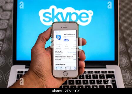 In dieser Abbildung wird eine Skype-App im App Store auf einem Smartphone-Bildschirm mit einem Skype-Logo auf einem Laptop im Hintergrund angezeigt. Stockfoto
