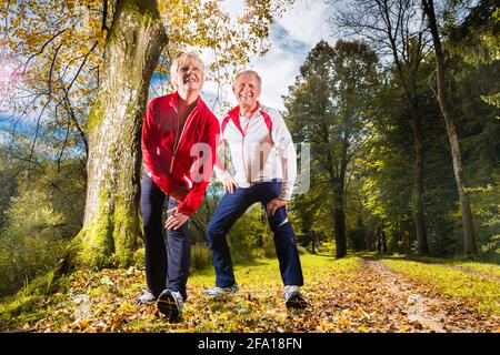 Senior paar tun erstreckt sich auf einem Waldweg im Herbst Stockfoto