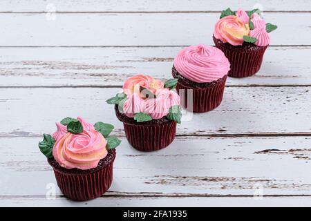 Vier rote Samt-Cupcakes mit rosa Buttercreme bedeckt. Auf einem weißen Tisch. Stockfoto