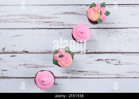 Vier rote Samt-Cupcakes mit rosa Buttercreme bedeckt. Auf einem weißen Tisch (Draufsicht). Stockfoto