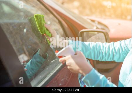 Autofensterreinigung. Weibliche Reinigung Autoscheibe mit Tuch und Sprühflasche. Nahaufnahme Bild, Frau, Fahrer, trocken wischen ihr Auto mit Mikrofaser c Stockfoto